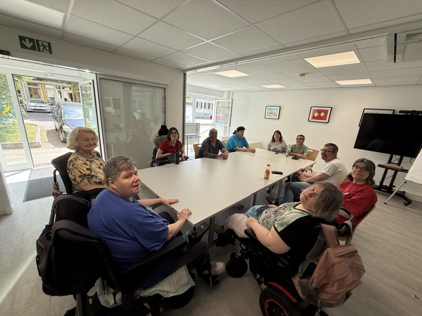 Eine Gruppe von Menschen mit und ohne Rollstuhl sitzt um einen Tisch in einem Konferenzraum.